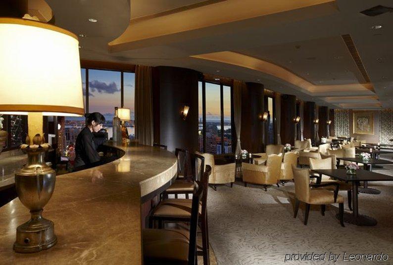 Ambassador Hotel Kaohsiung Restaurante foto The photo depicts an elegant bar or lounge area within a high-rise setting. The interior features warm lighting, with a large lamp illuminating the bar counter. There is a bartender seated at the bar, and the space includes plush chairs and tables ar
