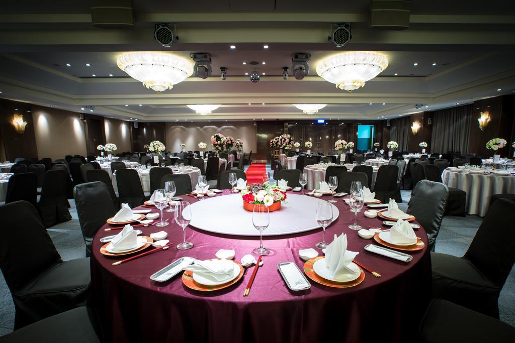 Ambassador Hotel Kaohsiung Exterior foto The photo depicts an elegantly set dining area for an event. 

In the foreground, there is a circular table covered with a dark red tablecloth, featuring a centerpiece of flowers in vibrant colors. The table is equipped with white plates, polished cu
