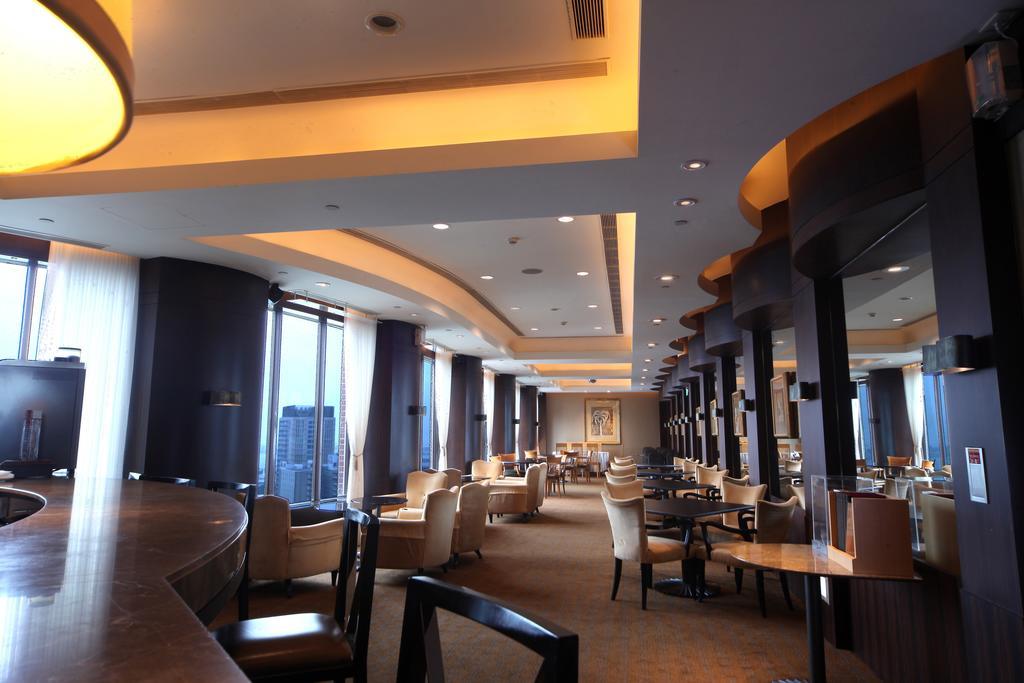 Ambassador Hotel Kaohsiung Exterior foto The photo shows the interior of a modern restaurant or lounge. The space features elegant seating with cream-colored chairs and wooden tables, arranged in a spacious layout. Soft, warm lighting highlights the architectural details of the ceiling and 
