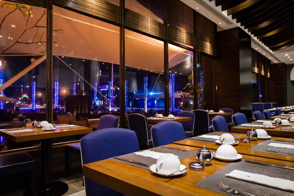 Ambassador Hotel Kaohsiung Exterior foto The photo shows the interior of a restaurant with a modern and elegant design. There are several tables set with white dishware and utensils, featuring a combination of dark wooden and blue upholstered seating. Large windows provide a view of a night