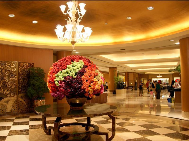 Ambassador Hotel Kaohsiung Exterior foto The photo shows the interior of a spacious lobby area, characterized by elegant design elements. In the center, there is a large round floral arrangement made up of vibrant flowers in various colors, displayed in a decorative vase on a dark, round ta