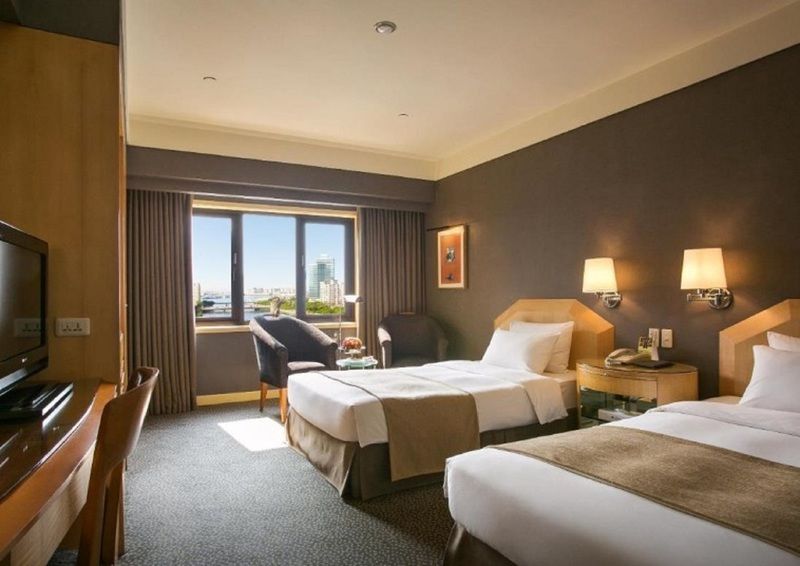 Ambassador Hotel Kaohsiung Exterior foto The photo shows a hotel room featuring two twin beds with beige and brown bedding. The room has a modern design with a dark accent wall and light-colored furniture. There are bedside lamps on each side of the beds, and a comfortable armchair is posit