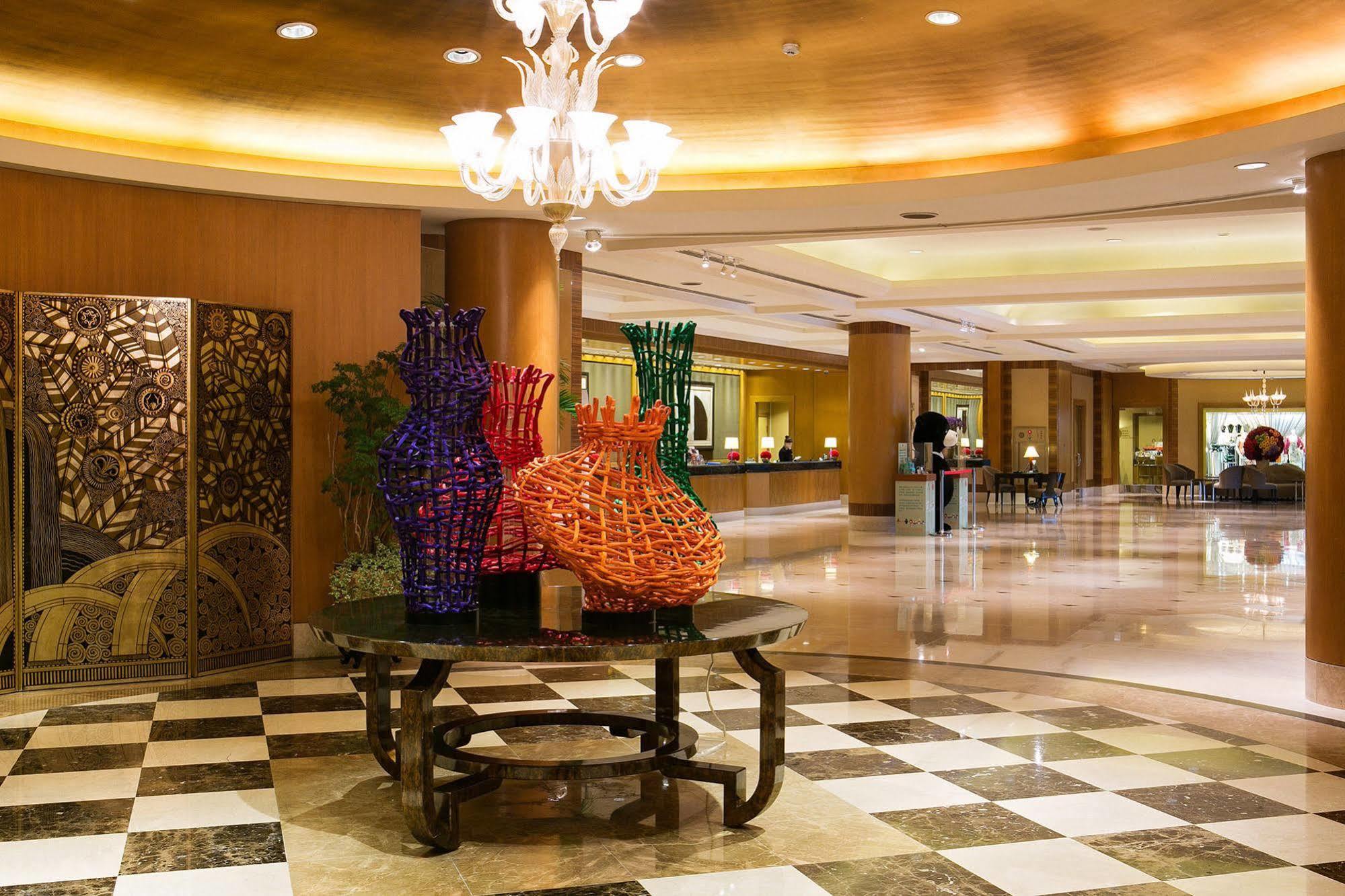 Ambassador Hotel Kaohsiung Exterior foto The photo shows the interior of a hotel lobby featuring an elegantly designed space. In the foreground, there is a decorative table with colorful woven vases, predominantly in purple and orange. These vases add a vibrant touch to the setting. The flo