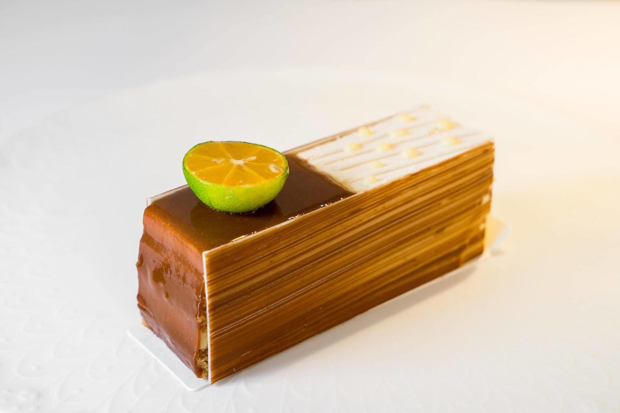 Ambassador Hotel Kaohsiung Exterior foto The photo shows a dessert that is shaped like a rectangular block or loaf. It features a glossy, golden-brown exterior, likely made with layers of chocolate or caramel. Atop the dessert, there is a halved lime slice, adding a pop of color and suggest