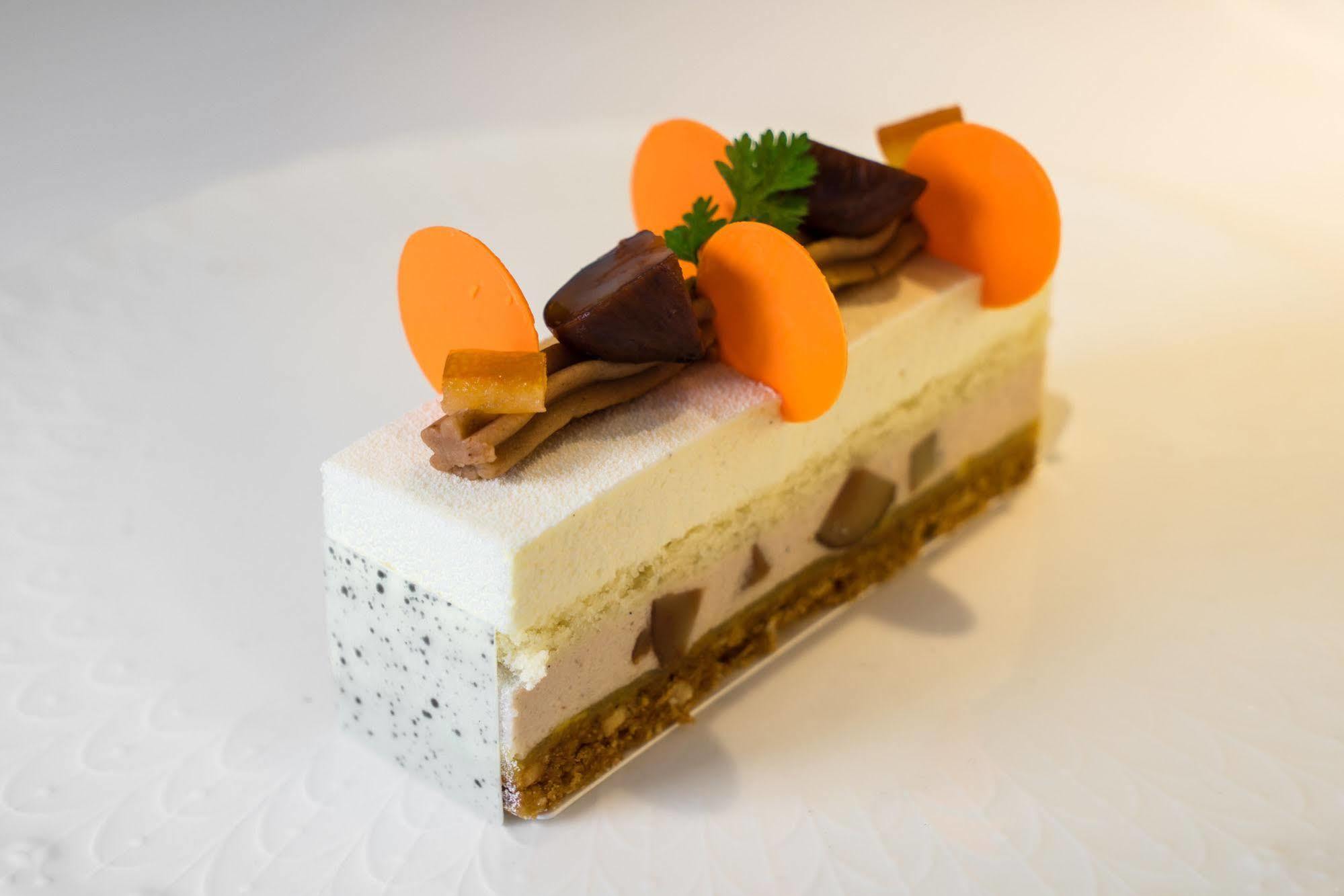 Ambassador Hotel Kaohsiung Exterior foto The photo features a dessert that appears to be a modern, layered cake or mousse. It has a rectangular shape and is composed of several distinct layers. The top layer is a light-colored mousse or cream, decorated with vibrant orange, circular element