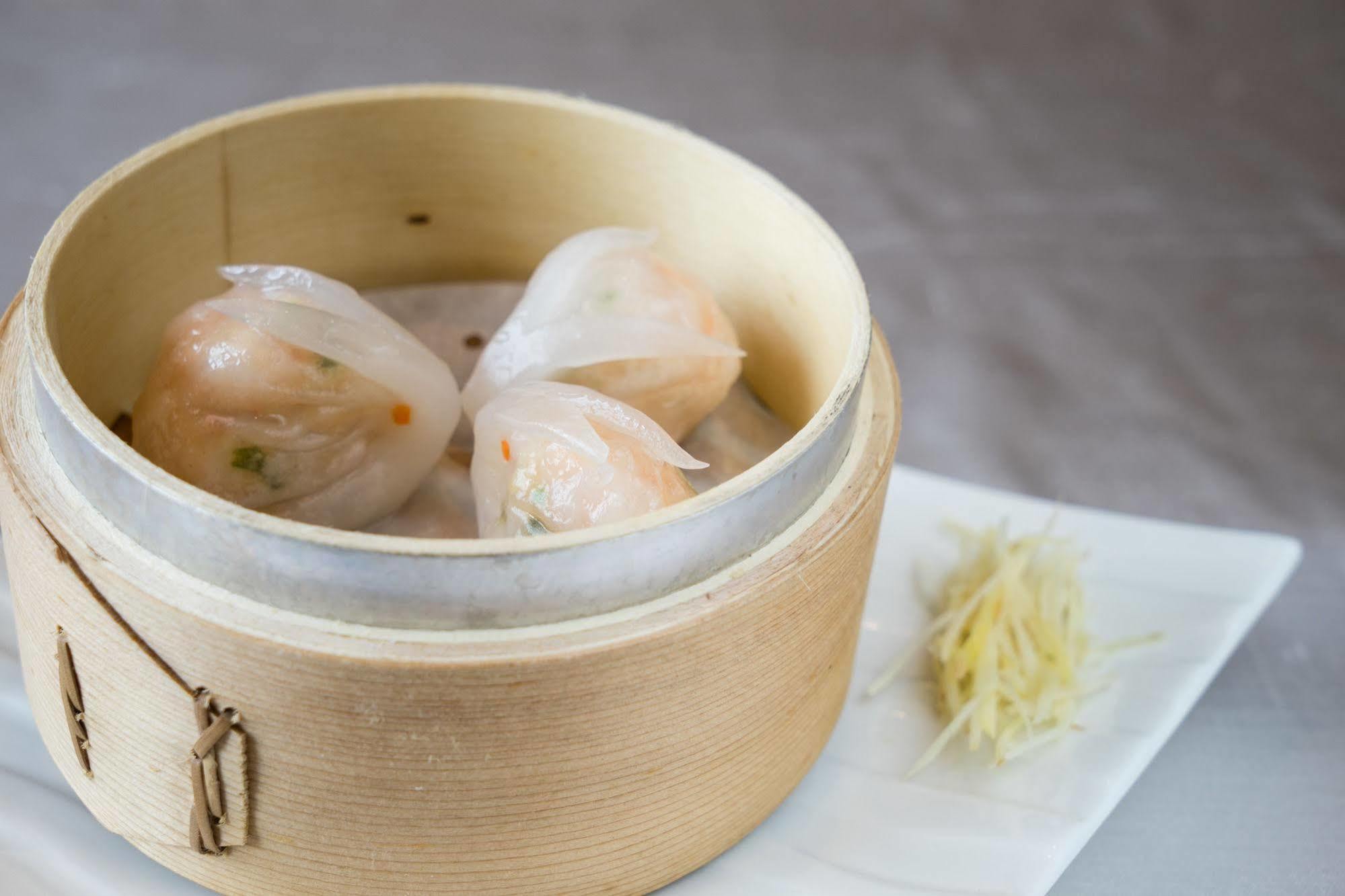 Ambassador Hotel Kaohsiung Exterior foto The photo shows a wooden steamer basket containing three pieces of dumplings, likely shrimp dumplings known as har gow. These dumplings are translucent, revealing bits of shrimp and vegetables inside. Next to the steamer, there is a small mound of sl