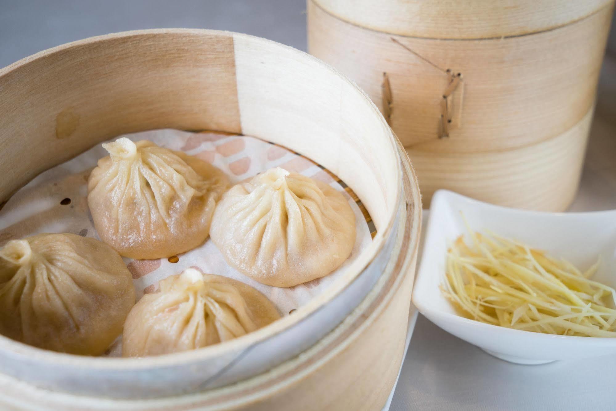 Ambassador Hotel Kaohsiung Exterior foto The photo shows a bamboo steamer containing several dumplings, known as xiaolongbao, which are soup dumplings traditionally filled with meat and broth. The dumplings are arranged neatly on a layer of parchment paper inside the steamer. Next to the st