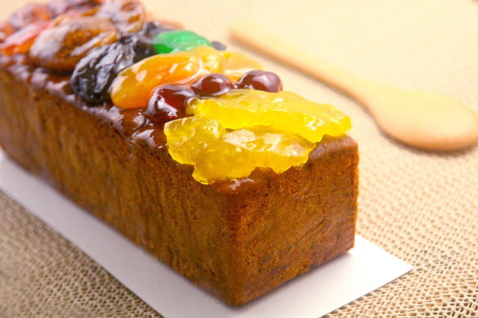 Ambassador Hotel Kaohsiung Exterior foto The photo shows a rectangular fruitcake that has a rich, dark color and is topped with an assortment of candied fruits. The toppings include brightly colored fruits like orange, green, and yellow, arranged attractively on top of the cake. The texture