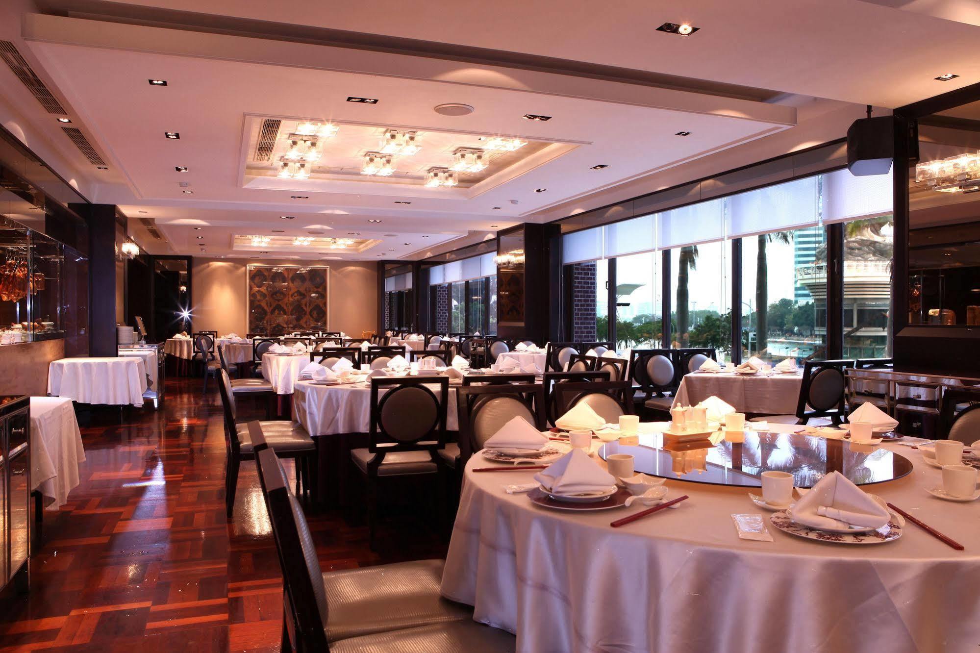 Ambassador Hotel Kaohsiung Exterior foto The photo shows an elegant restaurant interior. It features neatly arranged tables with white tablecloths and dining settings, including plates, cutlery, and folded napkins. The space is well-lit with ambient lighting and large windows that likely pr