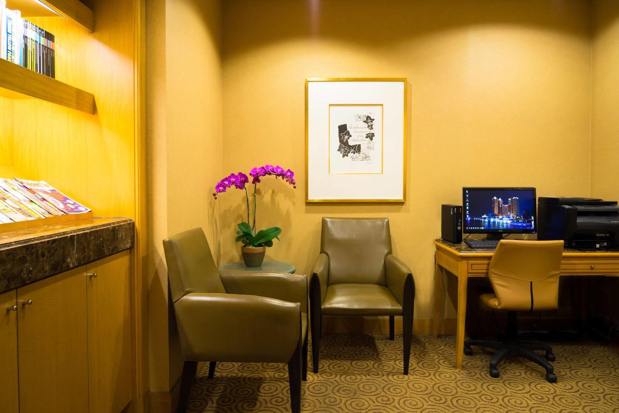 Ambassador Hotel Kaohsiung Exterior foto The photo shows a cozy corner of a room, which appears to be a waiting or lounge area. There are two stylish chairs positioned near a small table. A potted plant with purple flowers adds a touch of color and freshness to the space. On the wall, there