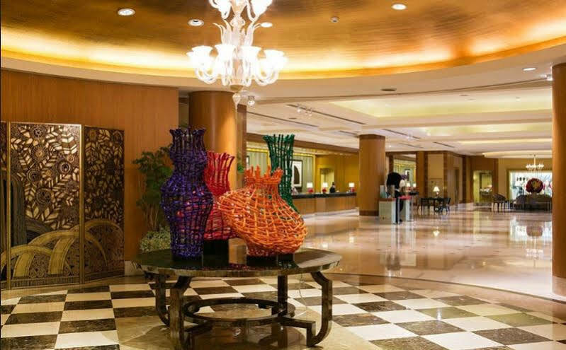 Ambassador Hotel Kaohsiung Exterior foto The image shows a spacious and elegantly designed lobby area. In the center, there are several large, artistic vases made of colorful materials, including shades of purple, orange, and green. These vases are displayed on a black table, contrasting wi
